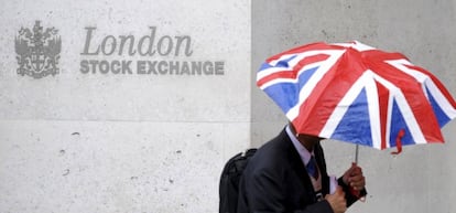 Un hombre con un paraguas con la bandera de Reino Unido pasa frente a la Bolsa de Londres.