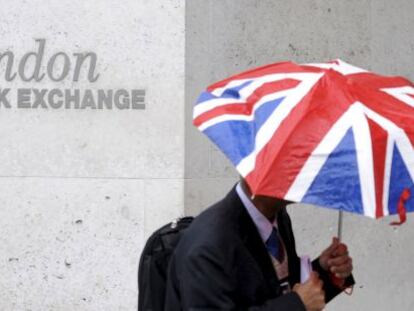 Un hombre con un paraguas con la bandera de Reino Unido pasa frente a la Bolsa de Londres.