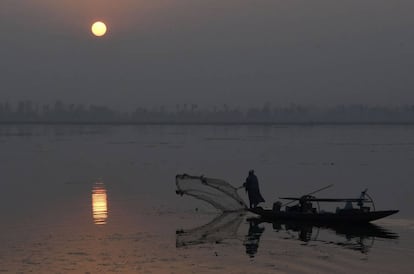 Un pescador de Cachemira arroja su red desde su bote durante una puesta de sol en el lago Dal en Srinagar.