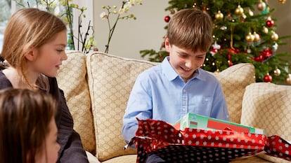 Un niños de 11 años abriendo un regalo en el sofá de sus casa.