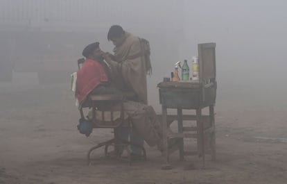 Un barbero paquistaní afeita a un cliente en las cercanías de una carretera de Lahore, rodeados de contaminación.