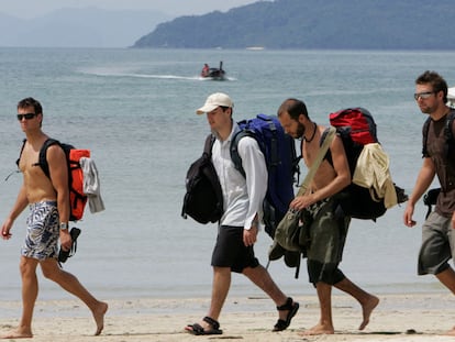 Chicos cargando mochilas caminando por la playa.