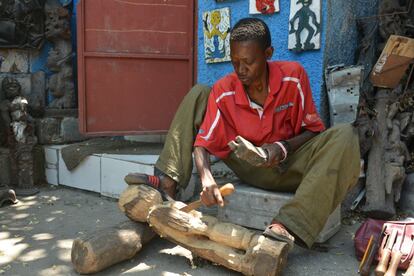 In this April 2, 2016 photo, sculptor Jean Robert Palanquet carves on a piece of wood in an open-air museum and art workshop off a trash-strewn street cutting through some of the poorest neighborhoods in Port-au-Prince, Haiti. Palanquet is a member of a collective of Haitian artists called Atis Rezistans who have become celebrated in the international art world by creating sculptures out of scrapped car parts, old wood, cast-off toys and even human skulls found scattered outside crumbling mausoleums. (AP Photo/David McFadden)