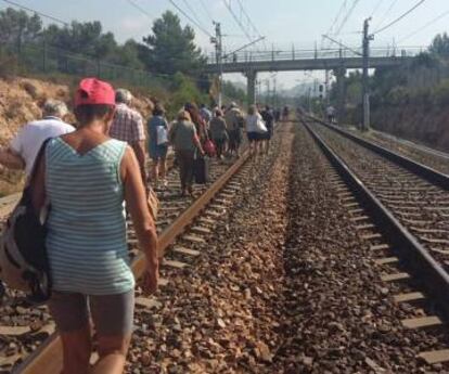 Passatgers d'un tren afectat caminen per les vies.