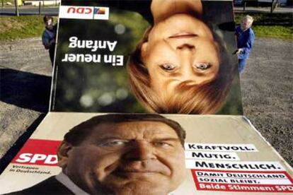 Dos hombres retiran los carteles electorales de Schröder y Merkel, que empataron ayer en las elecciones federales.