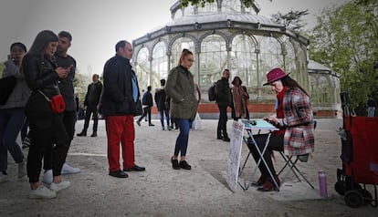 Varias personas esperan mientras Nuria Herrera escribe en el Retiro, este sábado.