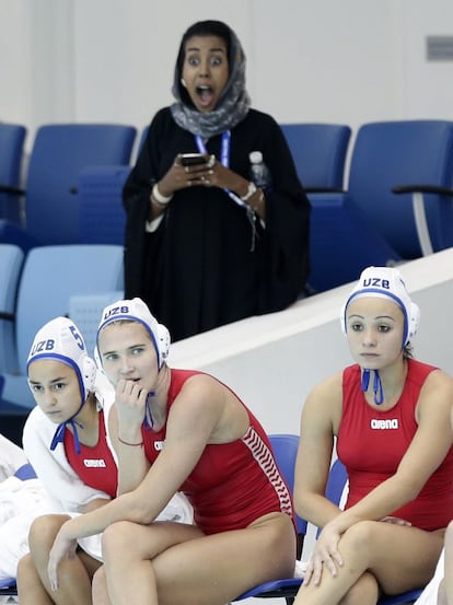 Una espectadora gesticula detr&aacute;s de tres jugadoras de Uzbekist&aacute;n durante el partido de waterpolo contra China en Dubai.