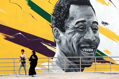 Unas mujeres pasan delante de un mural que representa al exjugador brasileño Edson Arantes do Nascimento, "Pelé" enfrente del estadio Al Khalifa de Doha, Catar, este viernes. EFE/Antonio Lacerda