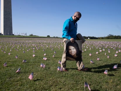 Um homem passa com um retrato de sua mãe, que morreu de covid-19, entre as milhares de bandeiras colocadas ao lado da base do obelisco de Washington em homenagem às vítimas do novo coronavírus, no dia 22 de setembro.