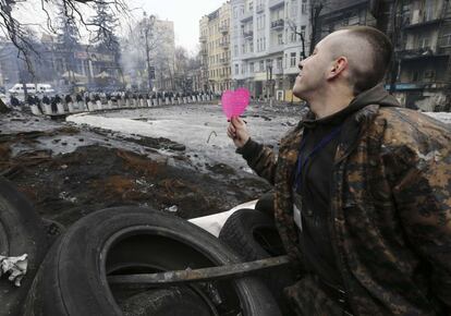 Un opositor al gobierno ucranio muestra un corazón de papel a los policías antidisturbios desde una de las barricadas de una calle de Kiev, con motivo del día de San Valentín.