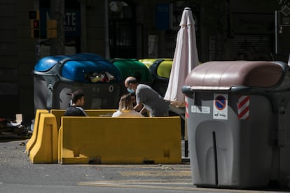 La terraza de un bar en pleno chaflán de la calle Aragón, entre contenedores de basura y reciclaje.