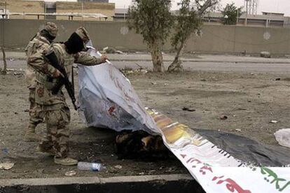 Miembros de la Guardia Nacional iraquí inspeccionan un cadáver, cubierto con una pancarta electoral, tras la explosión de un coche bomba al este de Bagdad.
