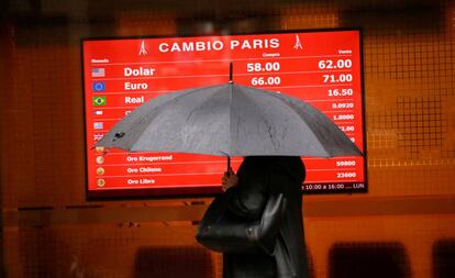 Una mujer que se protege de la lluvia pasa por delante de la pizarra de una casa de cambio de divisas.