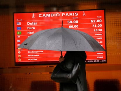 Una mujer que se protege de la lluvia pasa por delante de la pizarra de una casa de cambio de divisas. 