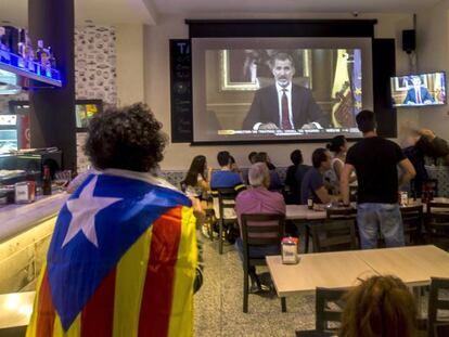 Varias personas escuchan en Barcelona el discurso del Rey.