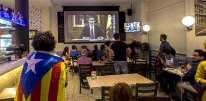 Varias personas escuchan en Barcelona el discurso del Rey.