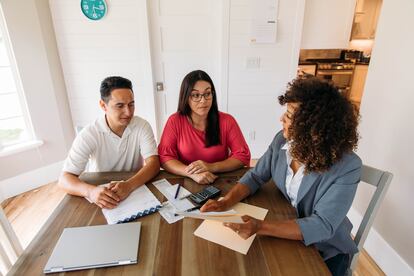 Una asesora se sienta con un matrimonio, les muestra a sus clientes cómo leer informes financieros y finanzas mensuales, pagar impuestos y ahorrar dinero para el futuro.