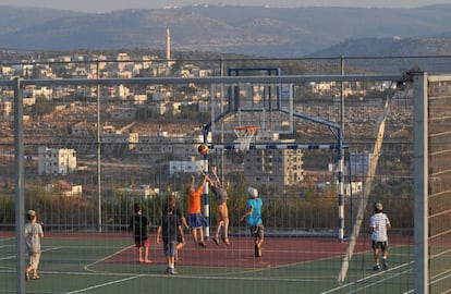 Niños colonos israelíes, con la aldea palestina de Burukin en el fondo, juegan al baloncesto en el asentamiento de Bruchin en Cisjordania.