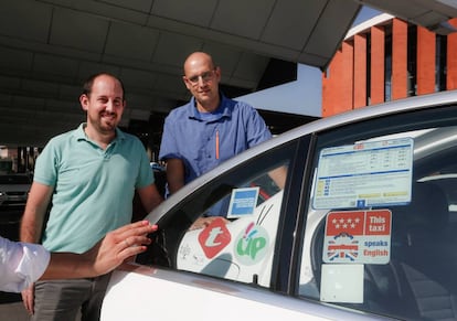 Los taxistas Daniel Elizo (izquierda) y Oscar López (derecha) posan en un taxi con la pegatina 'This taxi speaks English' que acredita su nivel básico de inglés.