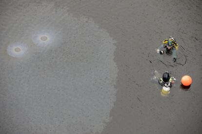 Dos buzos de la Guardia Civil junto a una mancha de aceite proveniente del vehículo de una conductora septuagenaria que se precipitó esta mañana al embalse de Bao y que ha resultado fallecida en el accidente ocurrido en el municipio orensano de Viana do Bolo.