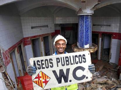 Un trabajador sostiene el cartel de los antiguos baños públicos de la plaza Urquinaona.