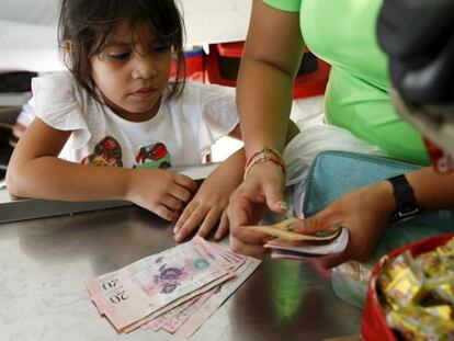 Uma criança olha enquanto sua mãe conta bolívares.