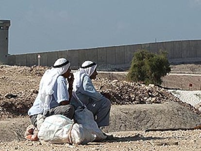 Dos palestinos observan un control israelí ante el muro de separación levantado en Cisjordania.