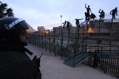 Un grupo de inmigrantes alcanza la verja fronteriza de Melilla ante la mirada de los policías españoles.