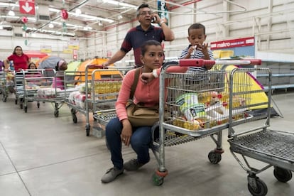 Un venezolano habla por su móvil mientras espera en la cola del supermercado.