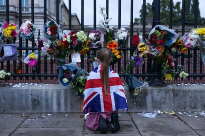 Una niña envuelta en la bandera británica observa los ramos de flores colocados en la verja del palacio de Buckingham, en Londres, este viernes. Isabel II falleció rodeada de su familia más cercana, que acudió a Balmoral (Escocia) cuando los médicos, a última hora de la mañana del jueves, informaron de que “preocupaba” su estado de salud.