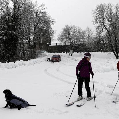 Dos esquiadores junto a un perro disfrutan entre la nieve del aparcamiento parking de Roncesvalles completamente cubierto.