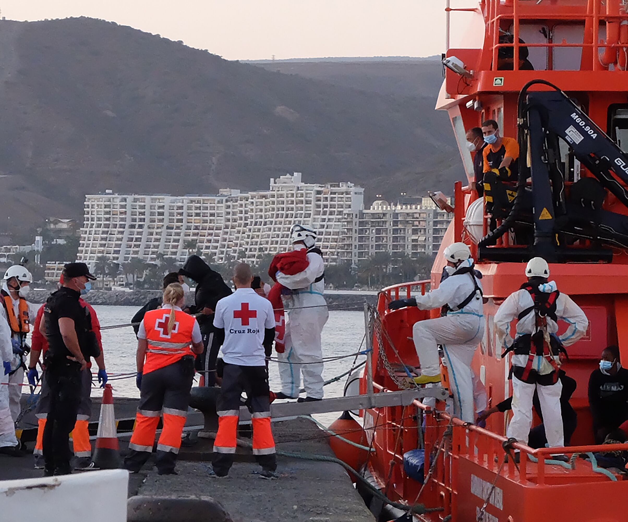 Miembros de la Cruz Roja ayudan a bajar del barco a migrantes en el puerto de Arguineguín (Gran Canaria, España) a 17 de marzo de 2021. 79 inmigrantes de origen subsahariano que viajaban a bordo de dos pateras fueron trasladados esa tarde noche por Salvamento Marítimo hasta el muelle de Arguineguín, en el Sur de Gran Canaria,  después de rescatarlos en alta mar. Entre ellos viajaban varios bebés, mujeres jóvenes y adultos. 