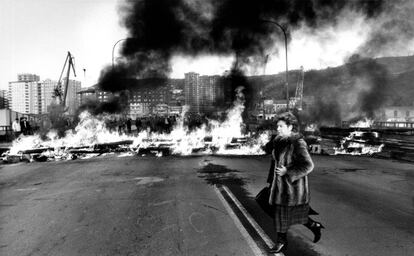 Una mujer con abrigo de piel pasa delante de una barricada en llamas en Bilbao.