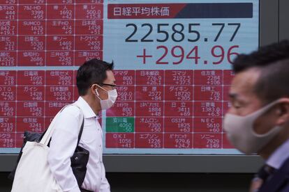 Dos hombres con mascarilla pasan ante un panel que muestra las cotizaciones de la Bolsa de Tokio, en Japón, el 13 de julio.
