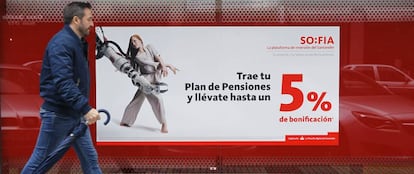 Una persona camina delante de una sucursal bancaria en la que se anuncian planes de pensiones. 