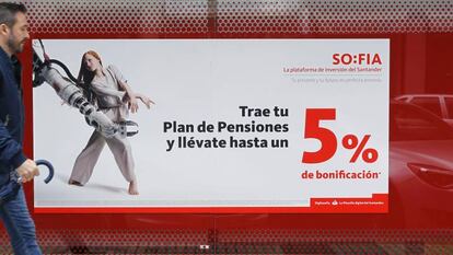 Una persona camina delante de una sucursal bancaria en la que se anuncian planes de pensiones. 