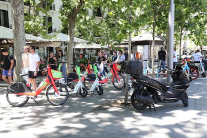 Patinetes, bicicletas y motos aparcados en una acera del centro de Madrid; al fondo, varias terrazas. 