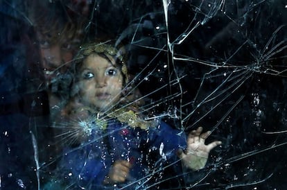 Una niña afgana desplazada mira a través de la ventana de su casa hecha de la luna rota de un automóvil en un barrio de Kabul, Afganistán.