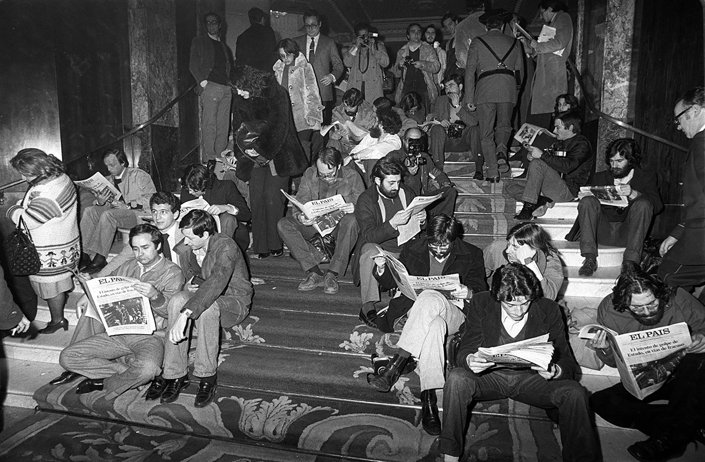 Periodistas de diversos medios fotografiados en las escaleras del Hotel Palace de Madrid, frente al Congreso de los Diputados, leyendo una de las siete ediciones del EL PAÍS durante la noche del Golpe de Estado del 23-F.