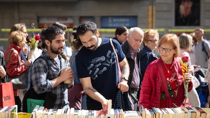 Varias personas de diferentes edades revisan la oferta de libros en uno de los puestos de la feria de Sant Jordi, en Barcelona.