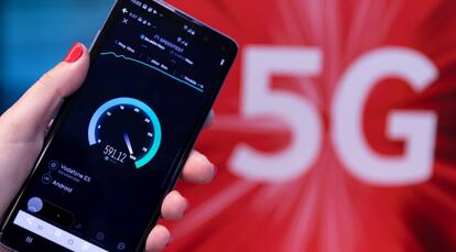 Una persona sostiene un teléfono móvil frente al logo del 5G.