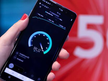 Una persona sostiene un teléfono móvil frente al logo del 5G.