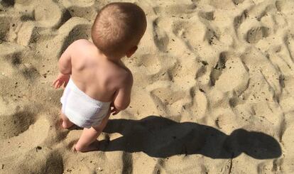 Un bebé en pañales juega en la playa.