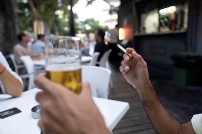 Una persona sostiene un cigarrillo en la terraza de un bar.