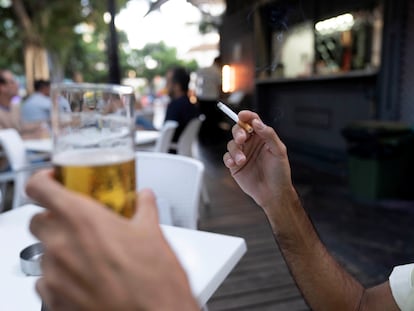 Una persona sostiene un cigarrillo en la terraza de un bar.