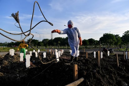 Dos trabajadores municipales realizan los últimos preparativos antes de enterrar a una víctima de covid-19, en un cementerio en Surabaya (Indonesia).