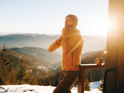 Un hombre abrochándose la chaqueta en un paraje invernal.