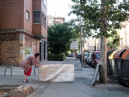 Una mujer arrastra un colchón hasta unos contenedores de basura en el barrio de Pan Bendito, en Carabanchel (Madrid).