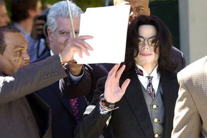 Michael Jackson saluda a la salida de la vista mientras su padre intenta protegerlo del sol con un papel.