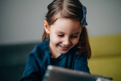 Una niña interactúa con su tableta en el sillón. 